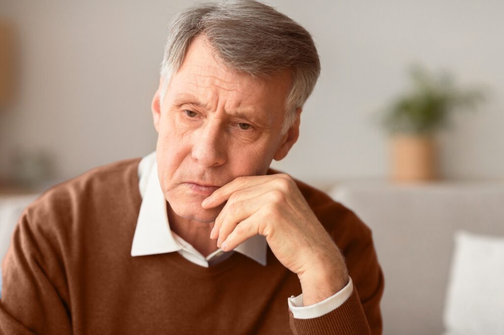 Portrait Of Depressed Senior Gentleman Thinking About Lonely Retired Life Sitting On Couch At Home. Selective Focus